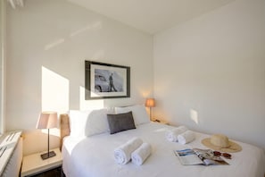 Ein Hotelzimmer mit einem Bett, einem Nachttisch mit Lampe, einem gerahmten Bild an der Wand und einem Fenster.