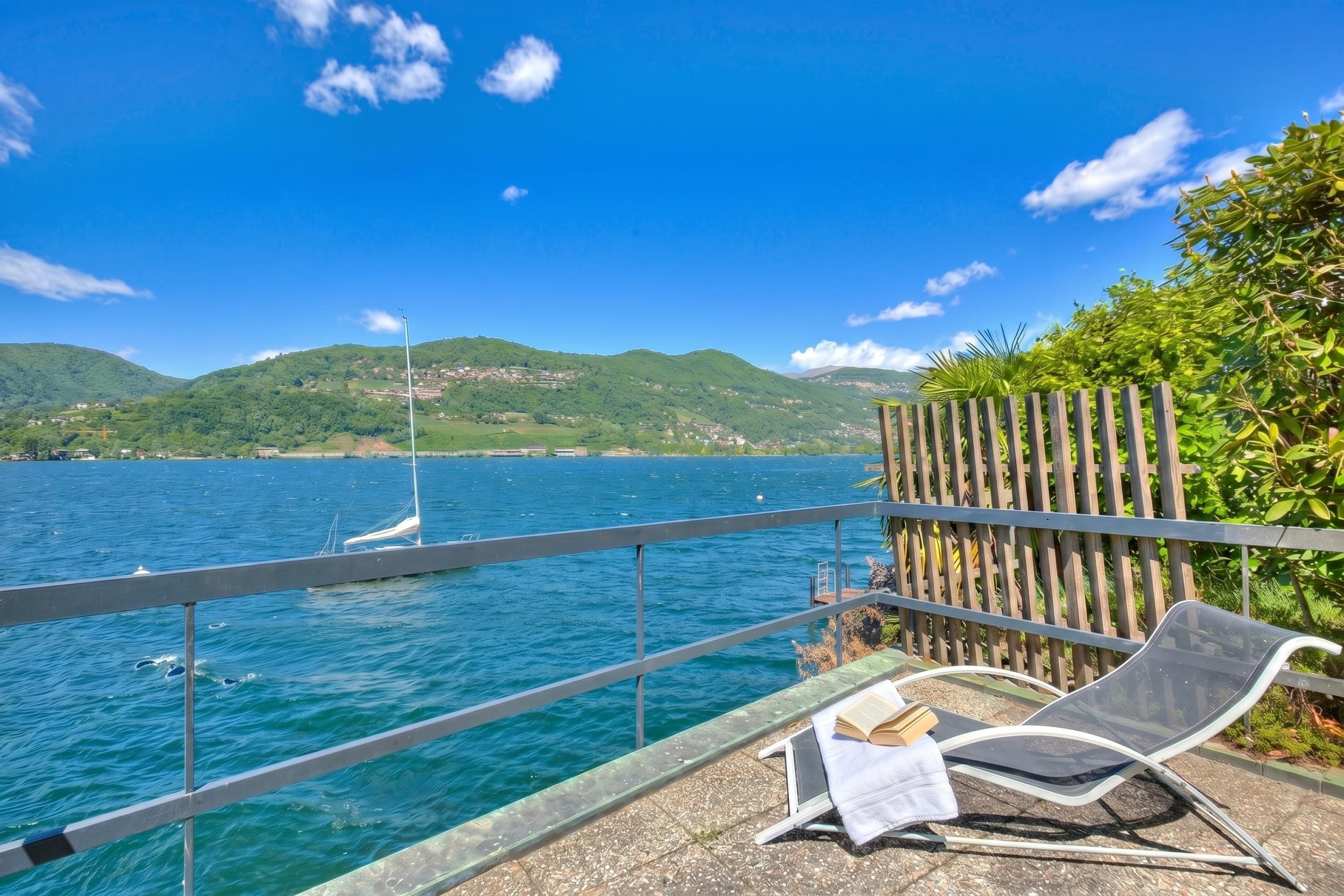 Merinäköala, jossa on tuoli ja avoin kirja, puisainen aita ja purjevene vedessä.
