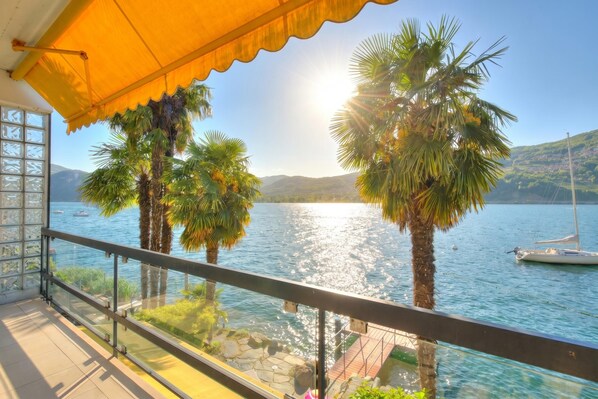Ein Balkon mit Glasgeländer, der auf einen See, Palmen und ein Boot blickt.