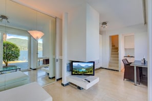 A modern living room with a flat-screen TV, a dining area, and a staircase leading to an upper level. - Bellariva On The Lake With View Balcony (Collina d'Oro)