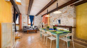 Un interior rústico con pared de piedra, vigas de madera, una mesa de comedor con sillas, un sofá y una chimenea.
