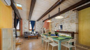 A dining area with a stone wall, wooden ceiling beams, and a table set for four. - Casa Rossa (Vrsar)