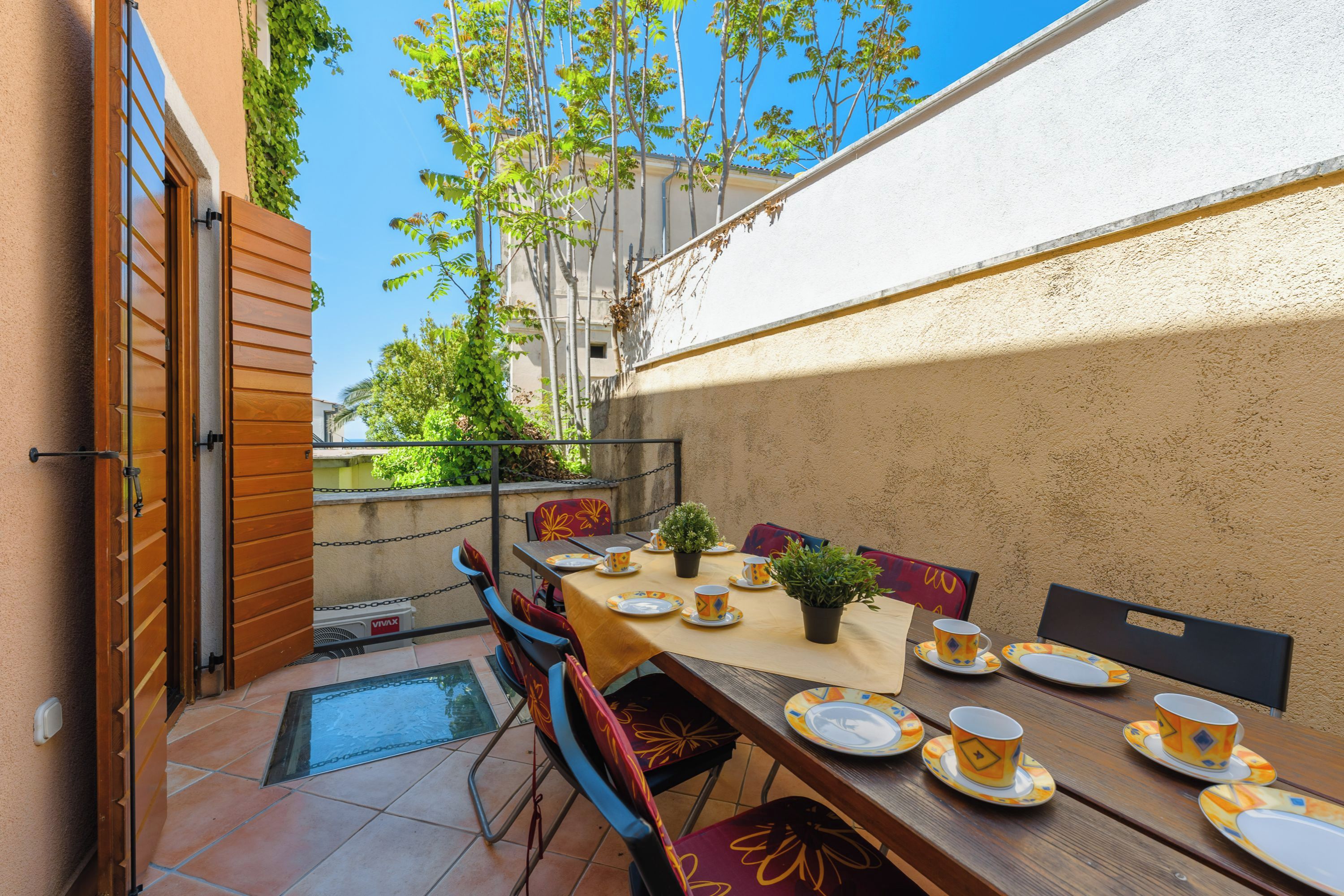 Un área de comedor al aire libre con una mesa dispuesta para cuatro, sillas y una planta en maceta.