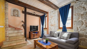 A living room with a sofa, a coffee table, a TV, and a stone wall. - Casa Rossa (Vrsar)