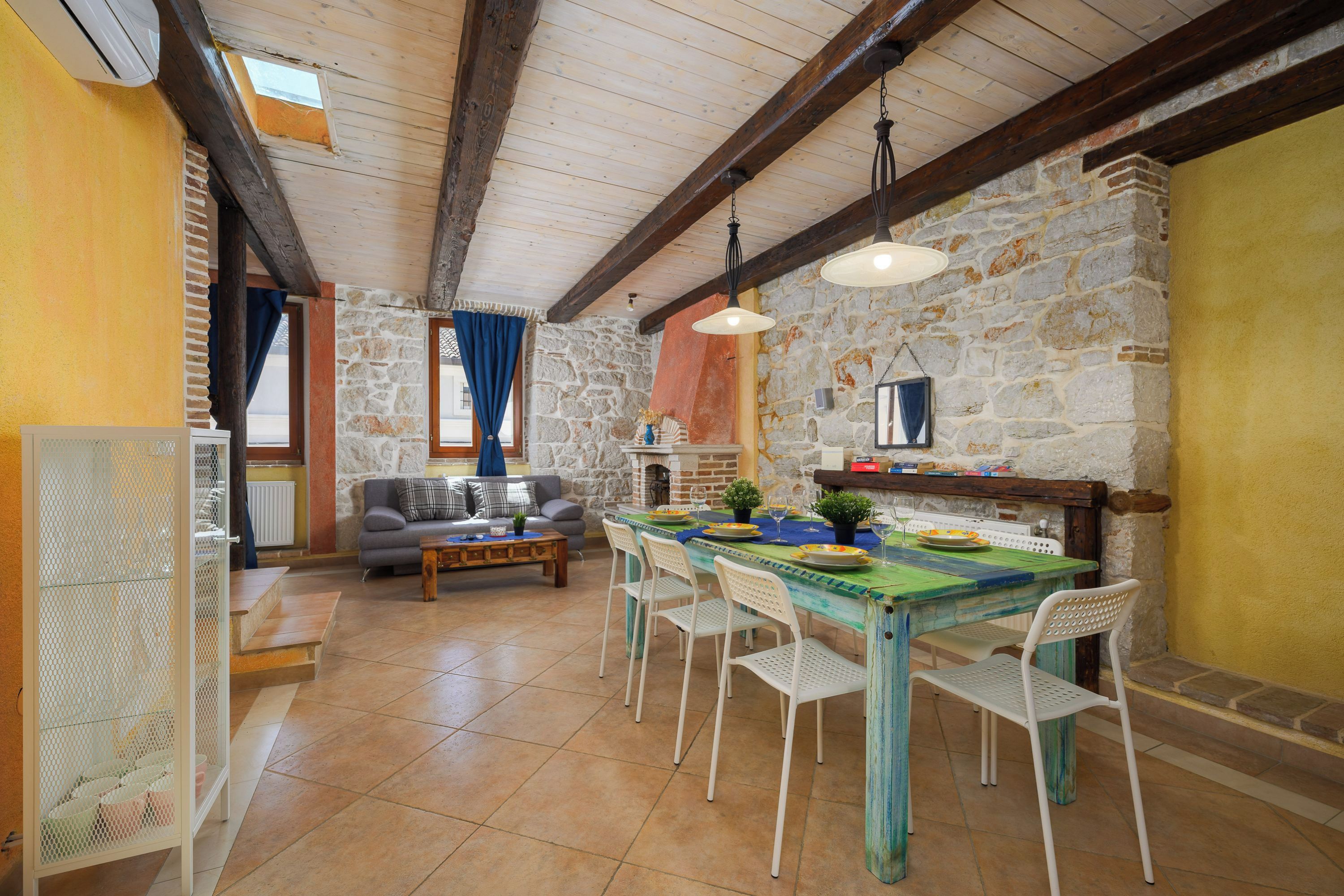 Comedor con pared de piedra, vigas de madera en el techo y una mesa lista para cuatro comensales.