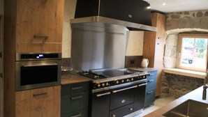 Cucina con forno a incasso, piano cottura e finestra affacciata su un muro in pietra.