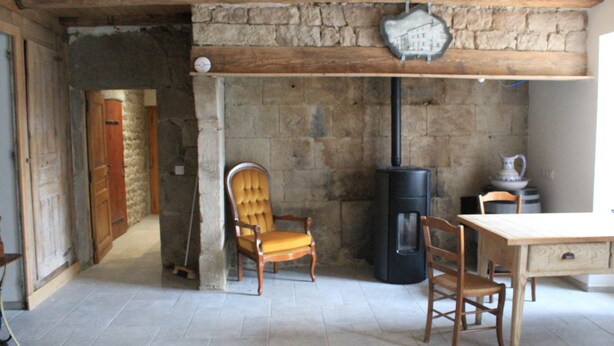 Una camera rustica con parete in pietra, soffitto in legno, camino, tavolo di legno e una sedia.