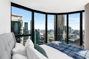 A bedroom with a city view, a bed with white and blue bedding, and a large window. - 2BR Skyline Apartment with Pool & Views (Southbank)