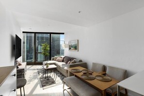 A modern living room with a sofa, a dining table, and a TV. - 2BR Skyline Apartment with Pool & Views (Southbank)