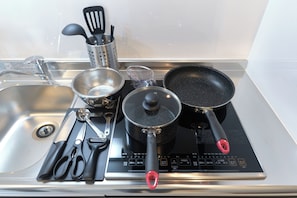 Eine Küche mit Herd, Töpfen, Pfannen, einem Sieb, einem Suppenlöffel und einem Pfannenwender.