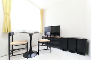 Ein modernes Zimmer mit Esstisch, zwei Stühlen, einem Fernseher und einem schwarzen Schreibtisch.