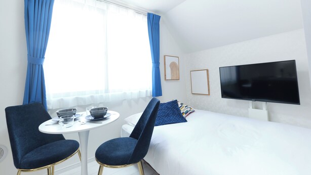 A hotel room with a bed, a TV, a dining table with chairs, and a window with curtains. - Fontaine Kamata by Tranova 2 (Ota City)