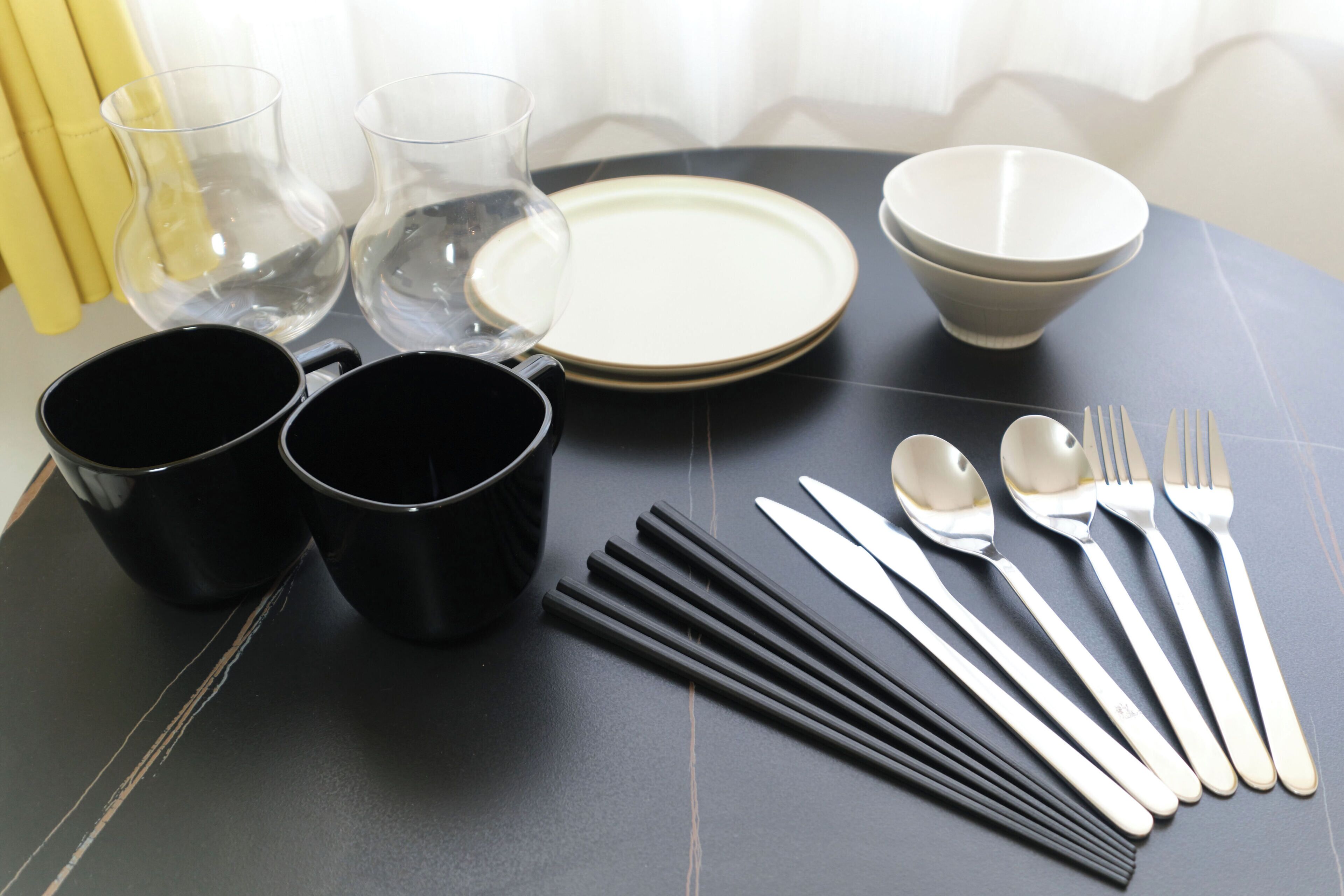 Una mesa dispuesta con vajilla blanco y negro, incluyendo platos, tazones, tazas y cubiertos.