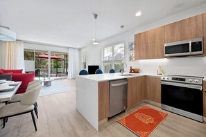 Eine moderne Küche mit Geschirrspüler, Mikrowelle und Backofen, ein Essbereich mit roten Stühlen und ein großes Fenster mit Blick auf eine Terrasse.