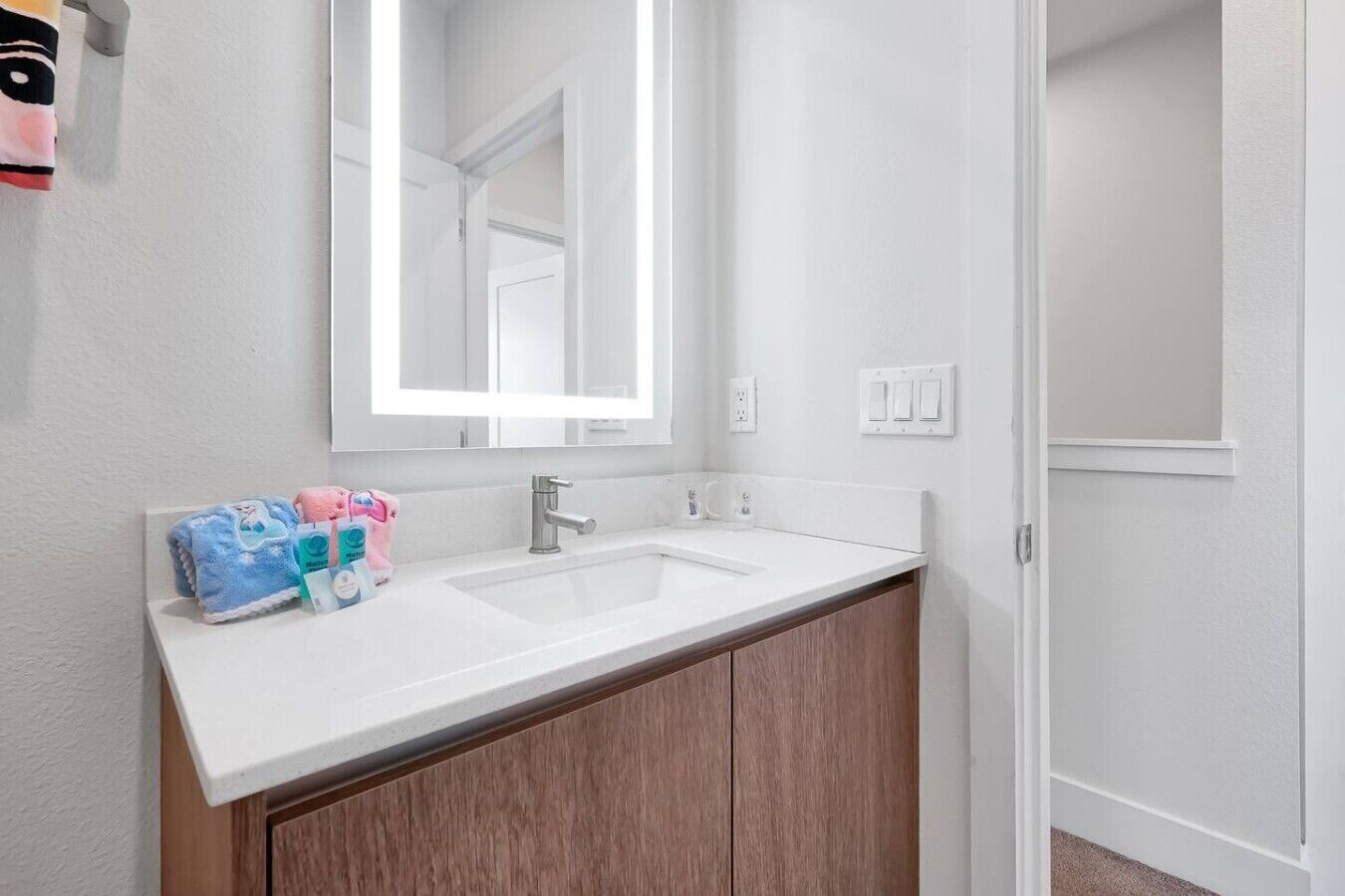 A bathroom with a white sink, wooden cabinets, a mirror, and toiletries on the counter.