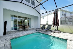 Une piscine entourée d’une enceinte de verre, avec des chaises longues et une table à proximité.