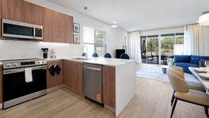 Una cucina moderna con forno a microonde, piano cottura e lavastoviglie integrati. C'è una zona pranzo con tavolo e sedie, e un divano blu nel soggiorno.