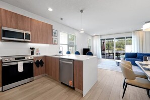 Eine moderne Küche mit integriertem Mikrowellenherd, Herd und Geschirrspüler. Es gibt einen Essbereich mit Tisch und Stühlen sowie ein blaues Sofa im Wohnzimmer.