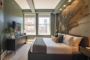 Ein modernes Schlafzimmer mit einem großen Bett, einem Schreibtisch, einer Topfpflanze und Blick auf die Stadt.