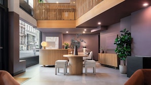 Et moderne receptionsområde med en træreception, to hvide polstrede stole, et rundt bord og en potteplante.