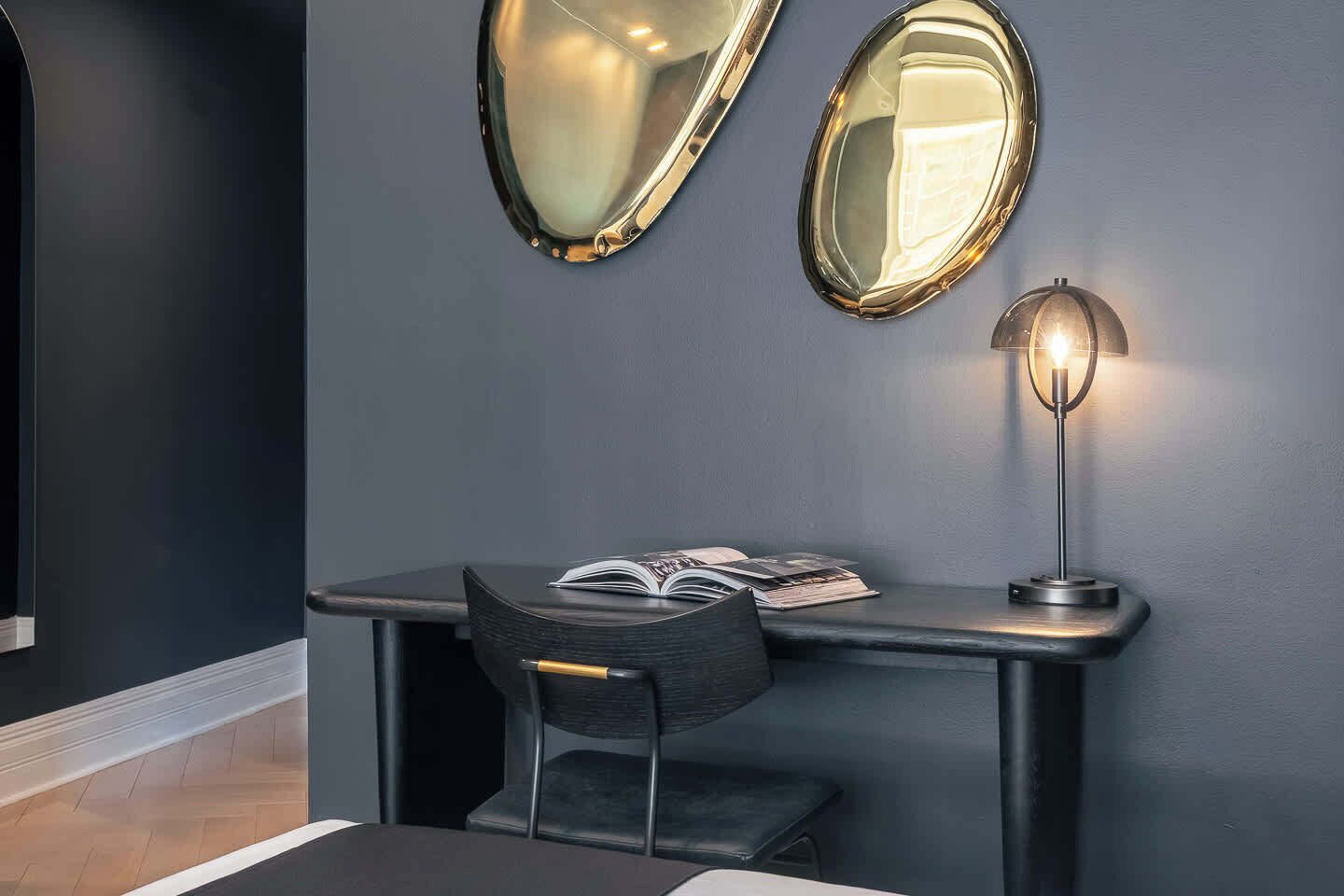 Een bureau met een stoel, een lamp en twee spiegels aan de muur.
