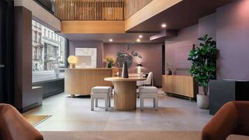 Una moderna zona de recepción con un mostrador de madera, dos sillones blancos con cojines, una mesa redonda y una planta en maceta.