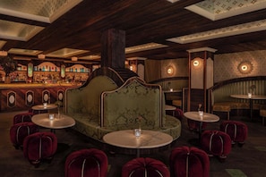 Een bar met een groen gestoffeerde zithoek, ronde tafels en rode fluweel ottomanen.