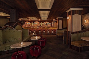 A bar area with a wooden ceiling, bar counter, and seating with round tables and red upholstered chairs. - NoMad Hotel Near Broadway & 5th Ave (New York)