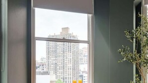 A dining area with a table and chairs, a window with a view of buildings, and a potted plant. - NoMad Hotel Near Broadway & 5th Ave (New York)