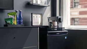 A coffee machine, a framed coffee menu, and a shelf with cups and bottles in a modern room with a window. - Madison Square Studio at Return Policy Broadway (New York)
