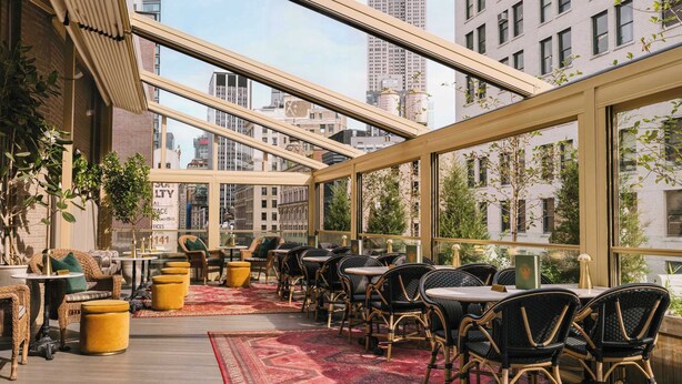 A rooftop restaurant with outdoor seating, large windows, and a view of city buildings. - Madison Square Studio at Return Policy Broadway (New York)