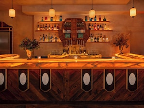 Una zona de bar con estantes de madera llenos de botellas, una encimera de mármol y espejos decorativos.