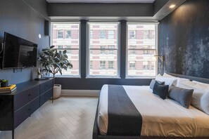 Une chambre moderne avec un grand lit, une télévision, une plante et une vue sur un immeuble en briques.