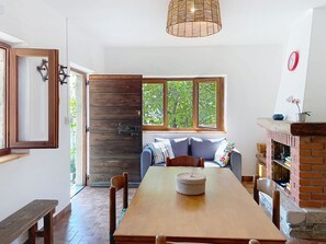 A dining area with a wooden table, chairs, a bench, a sofa, a fireplace, and a window with a view of trees. - La Baita dei Nonni by Interhome (Gera Lario)