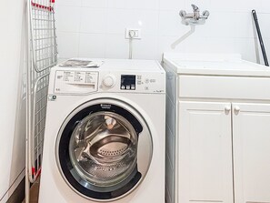 Eine Waschmaschine mit Frontlader, einer Bedienblende, einer weißen Fliesenwand und einem weißen Schrank.