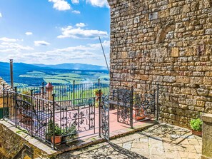 Eine Steinmauer mit einem Metallgitter und einer Bank, mit Blick auf eine schöne Landschaft mit Feldern und fernen Bergen.