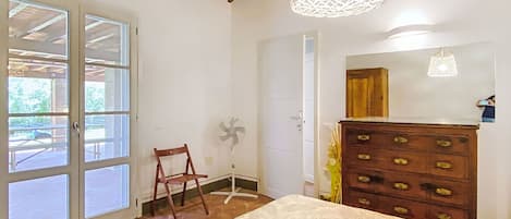 A bedroom with a wooden ceiling, a bed with a patterned bedspread, a dresser with drawers, a chair, and a fan.