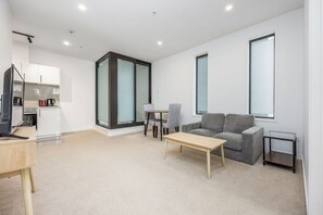 A modern living room with a sofa, a coffee table, and a dining area with chairs. - CBD Auckland Apartment (Auckland)