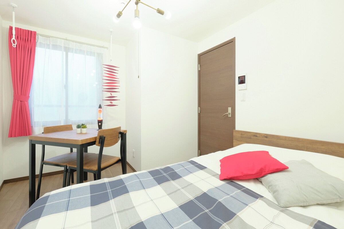 A bedroom with a bed, a wooden headboard, a bedside table with a lamp, a chair, and a window with curtains.