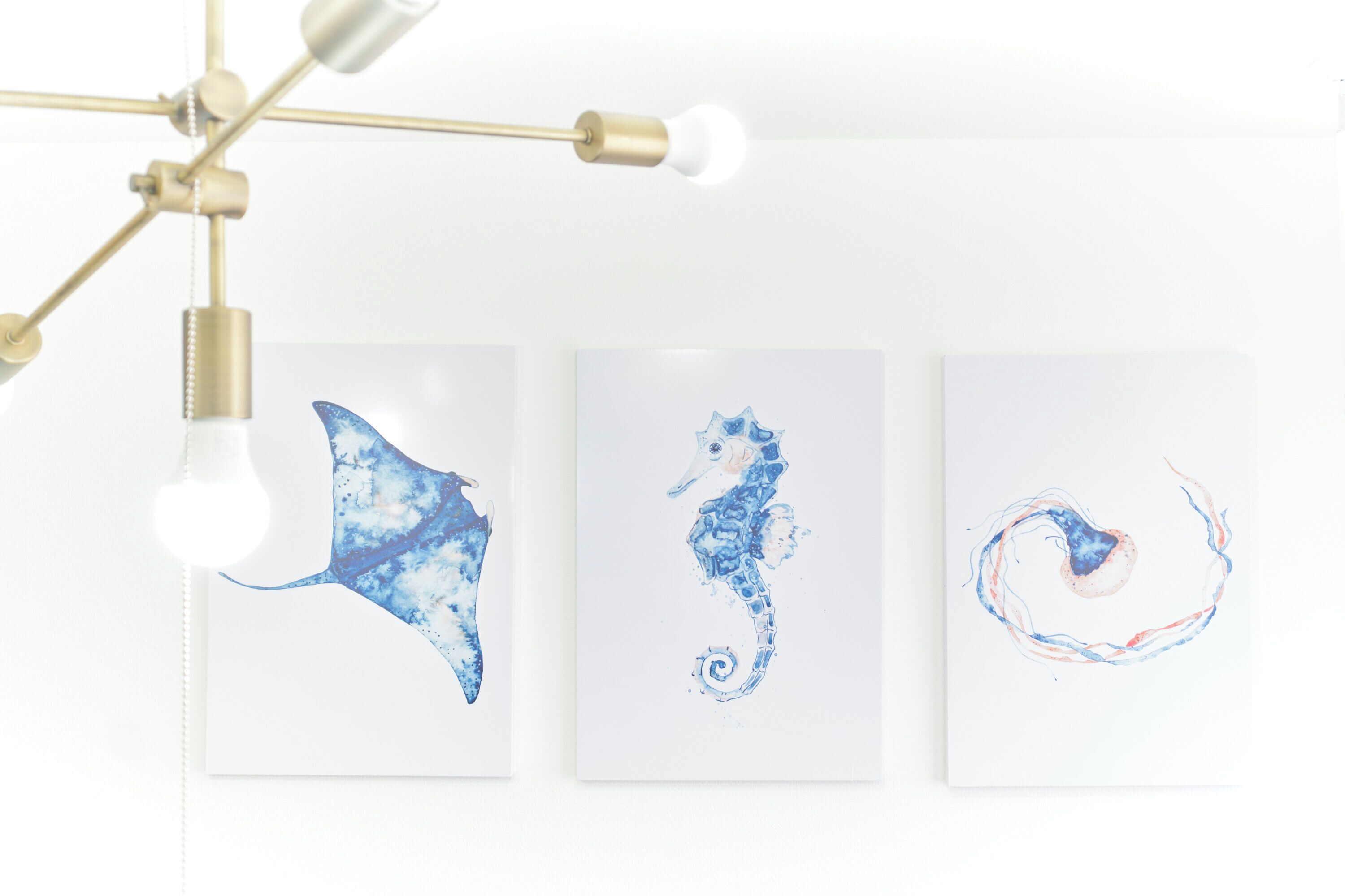 Three framed artworks on a wall, a ceiling light fixture, and a hanging light bulb.