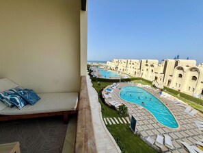 Ein Balkon mit Blick auf einen Poolbereich, Liegestühle und ein Gebäude im markanten architektonischen Stil.