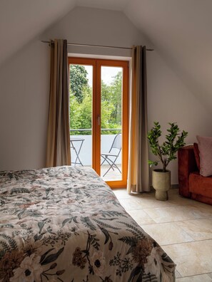 A bedroom with a bed, a potted plant, a chair, and a balcony with a table and chairs. - Rotes Haus am See - Dogs Welcome! (Lohmen)