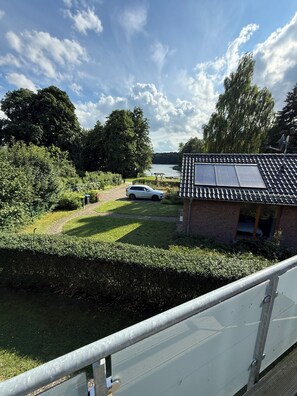 A residential area with a house featuring solar panels, a pathway leading to a parked car, and a lake in the background.