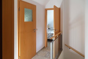 A wooden door with a frosted glass panel, a hallway with a tiled floor, and a bed with a floral bedspread in the background. - Rotes Haus am See - dogs welcome! (Lohmen)