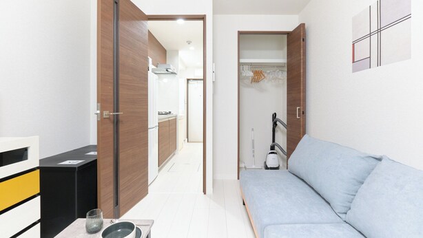 A compact room with a sofa, a table with a bowl and glass, and a hallway leading to a kitchen. - GRANQUAL Horikiri by Tranova 2 (Adachi)