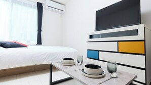 A hotel room with a bed, a table with plates and cups, an air conditioning unit, and a TV on the wall. - GRANQUAL Horikiri by Tranova 2 (Adachi)