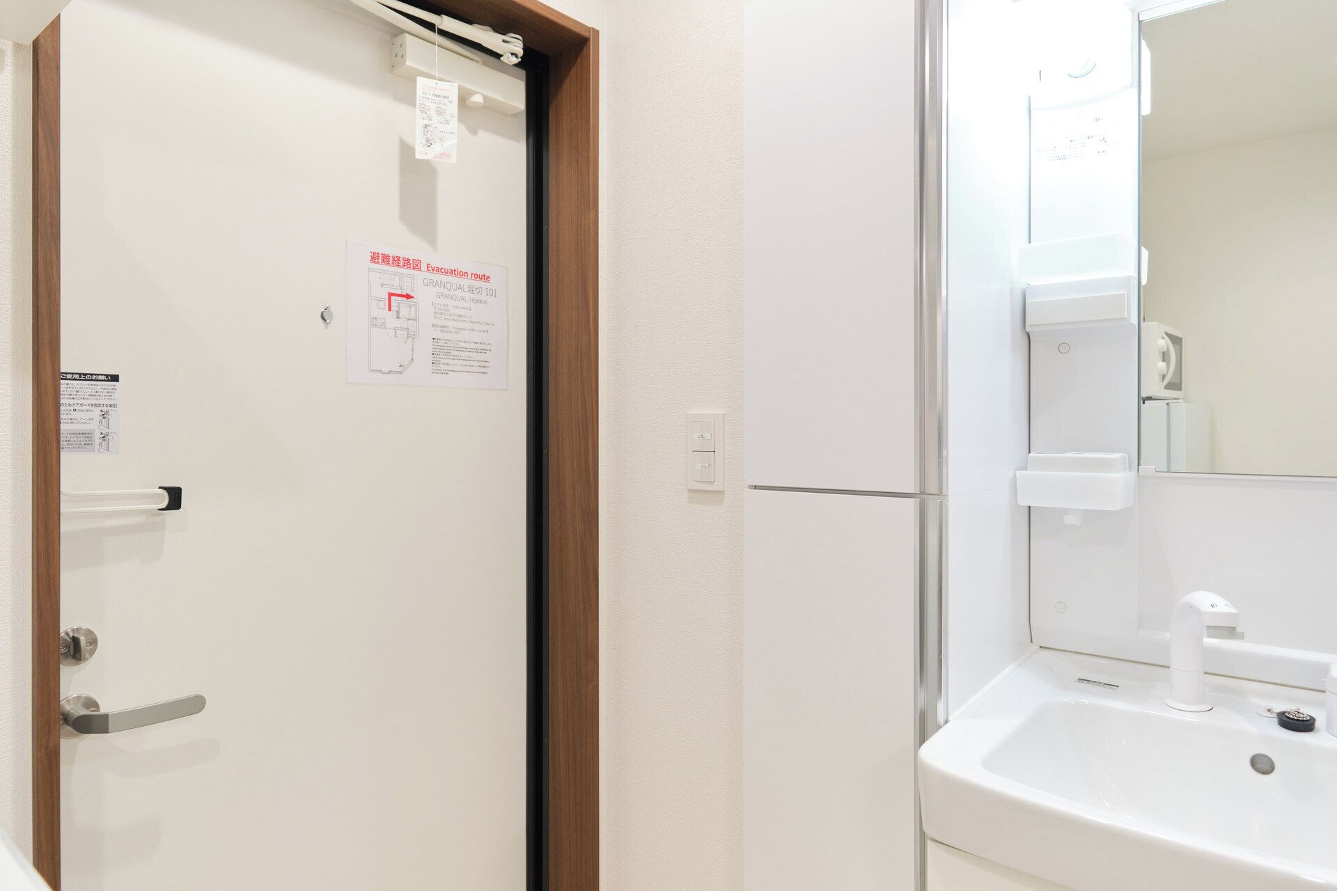A hotel room with a white door, a wooden frame, a white wall, a white sink, and a mirror.
