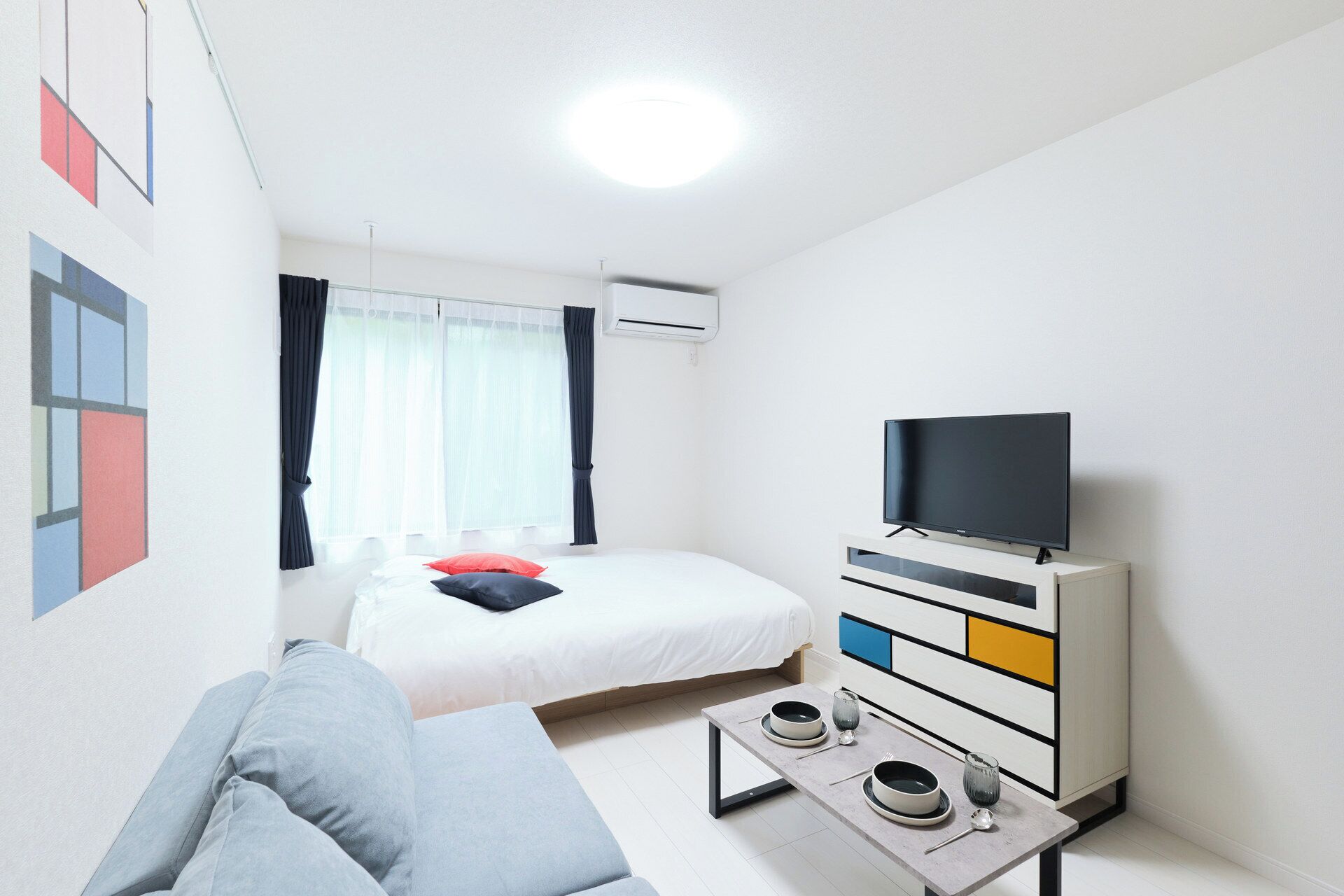 Une chambre d’hôtel moderne équipée d’un lit, d’une télévision, d’un canapé et d’une table à manger avec des bols et un verre.