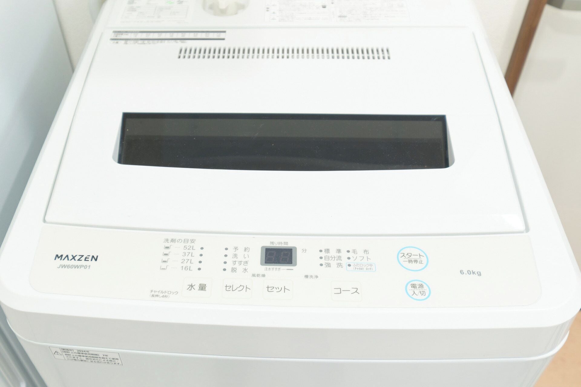 Une machine à laver blanche, dotée d’étiquettes en japonais, d’un écran numérique et d’un panneau de commande avec des boutons.