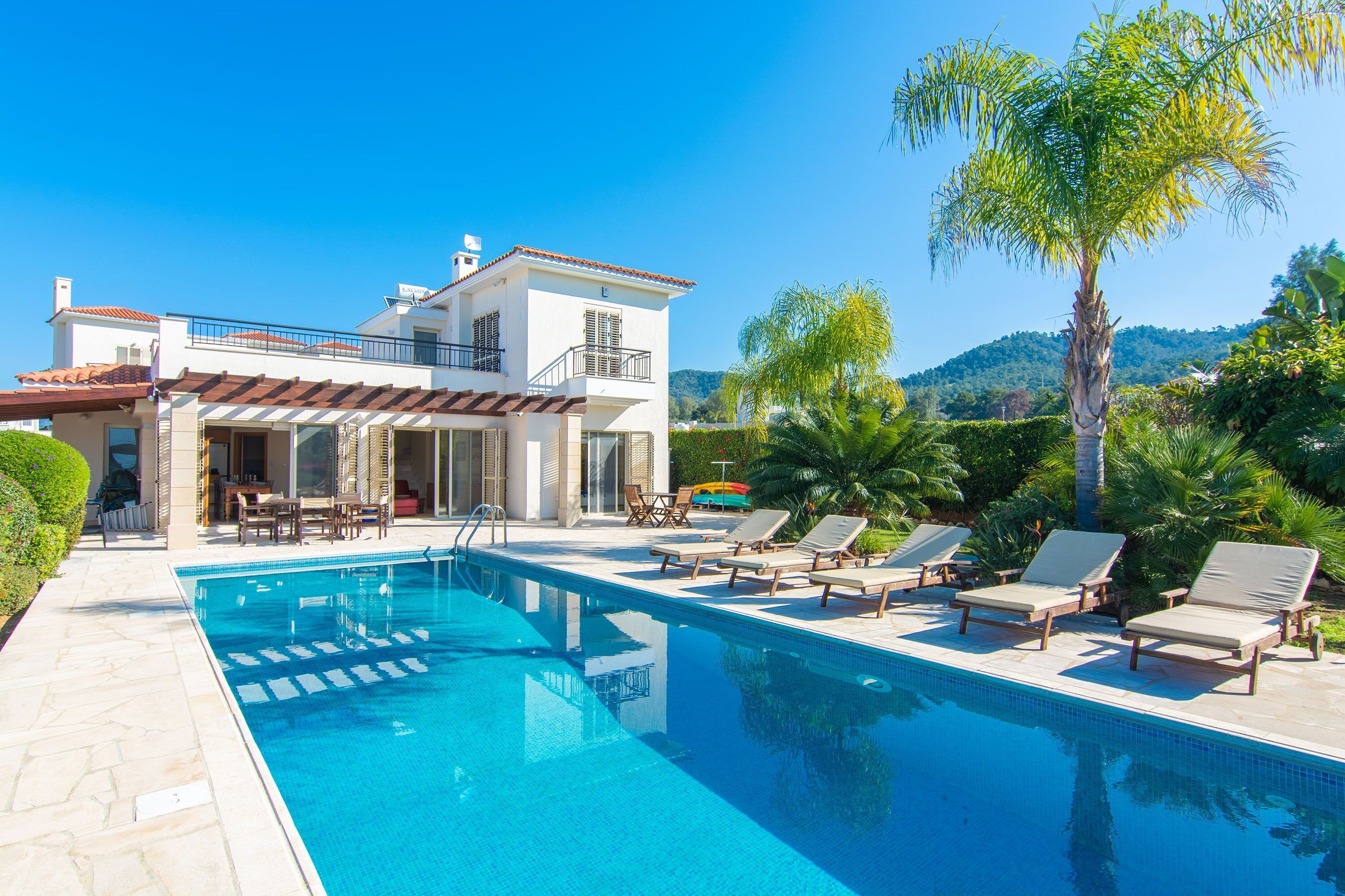 A modern house with a swimming pool, sun loungers, and a patio area.